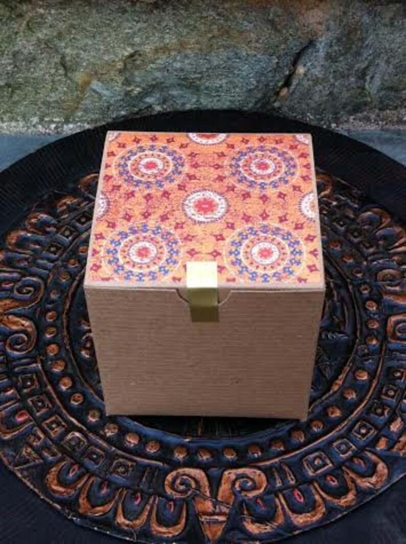 May include: A square gift box with a brown cardboard exterior and a colorful patterned top. The pattern features red, orange, blue, and white circular designs.