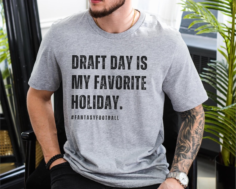 May include: A gray t-shirt with the text "Draft Day is My Favorite Holiday." and the hashtag "#FantasyFootball" printed on the front.