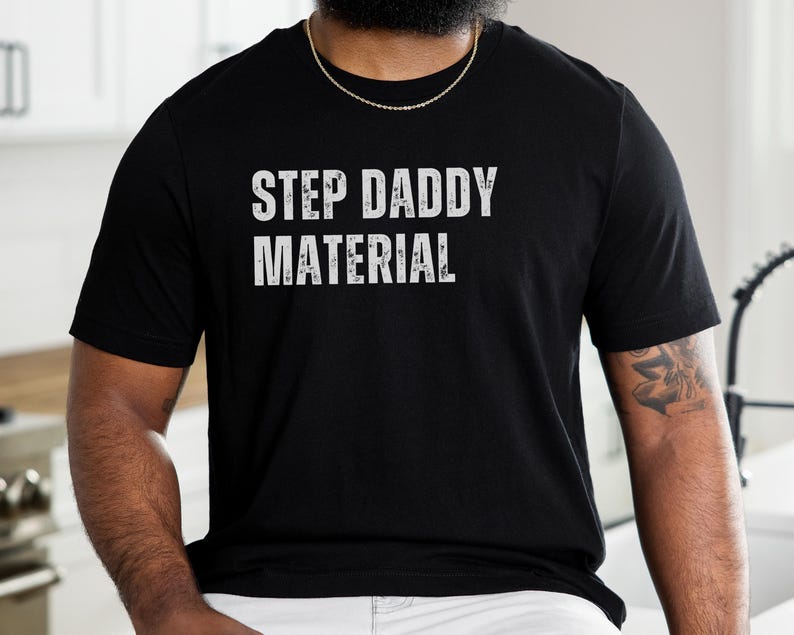 K&ouml;nnte beinhalten: Schwarzes T-Shirt mit wei&szlig;em Text, der "Step Daddy Material" lautet.