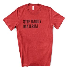 K&ouml;nnte beinhalten: Rotes T-Shirt mit kurzen &Auml;rmeln und dem Aufdruck "STEP DADDY MATERIAL" in Schwarz.