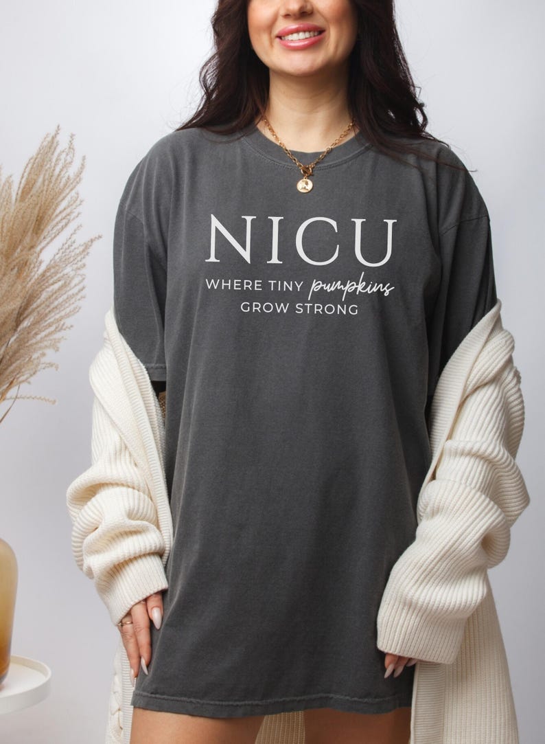 Puede incluir: Una camiseta gris oscuro con el texto "NICU Where Tiny Pumpkins Grow Strong" impreso en blanco.