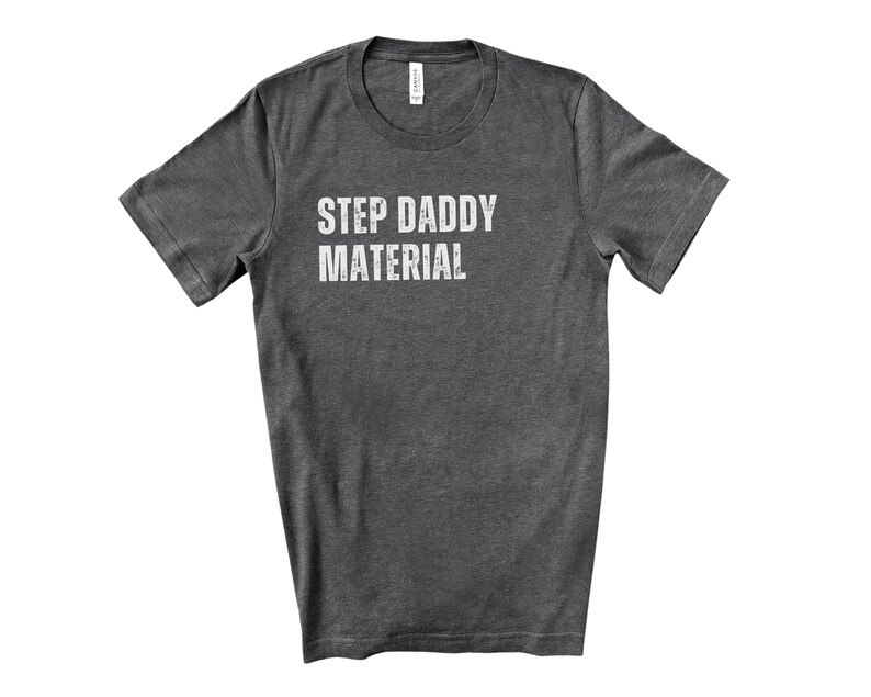 K&ouml;nnte beinhalten: Ein dunkelgraues T-Shirt mit dem Aufdruck "Step Daddy Material" in Wei&szlig;.