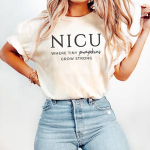 Puede incluir: Una camiseta blanca con el texto "NICU Where Tiny Pumpkins Grow Strong" impreso en la parte delantera.