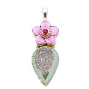 May include: A pendant featuring a five-petaled light pink flower with a small red center stone, attached to a teardrop-shaped iridescent druzy stone. The entire piece is set in a metallic frame with a silver-toned bail at the top for hanging.