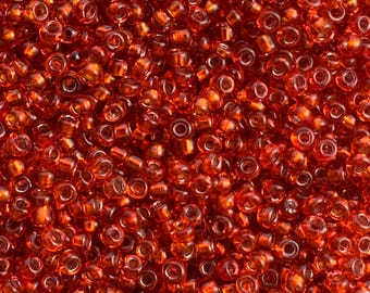May include: Close-up of a pile of small, transparent, red glass beads. The beads are cylindrical with a hole running through the center. The color is a vibrant, translucent red, with a slight orange hue. These beads are suitable for jewelry making and crafts.