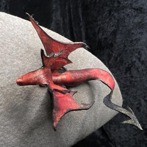 May include: A red leather dragon figurine with black accents. The dragon is in a flying pose with its wings spread out.