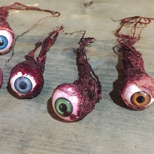 May include: Seven fake eyeballs with different colored irises, wrapped in bloody gauze, hanging from a string. The eyeballs are a Halloween decoration.