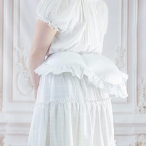 May include: A white, tiered skirt with ruffled trim and a matching white top. The outfit includes a ruffled bustle, creating a layered effect. The clothing is made of a lightweight fabric, suitable for a vintage or romantic aesthetic.