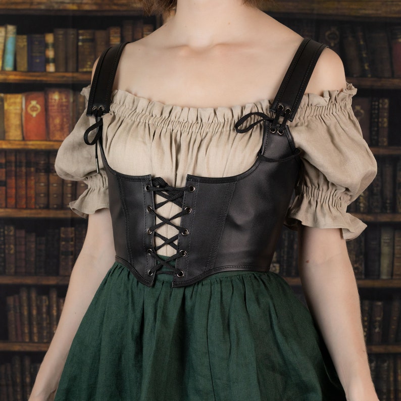 Leather underbust corset belt worn over beige peasant top and green skirt, shown against vintage library background