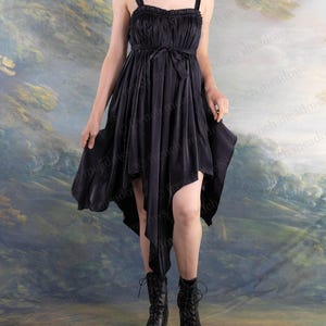Puede incluir: Vestido negro con dobladillo asim&eacute;trico. El vestido tiene un corpi&ntilde;o fruncido, tirantes finos y un cintur&oacute;n anudado. La persona lleva botas negras con cordones y un collar gargantilla negro.