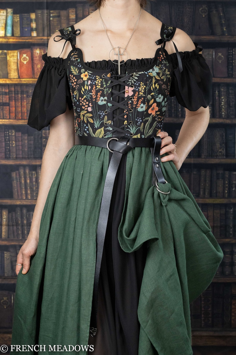 A black and green dress with a floral print bodice and a long, flowing skirt. The dress has a lace-up bodice and a belt with a buckle and skirt hikes