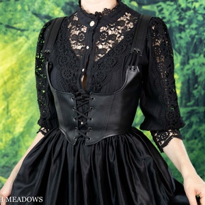 Black leather underbust corset belt styled with lace top and flowing skirt against green forest backdrop