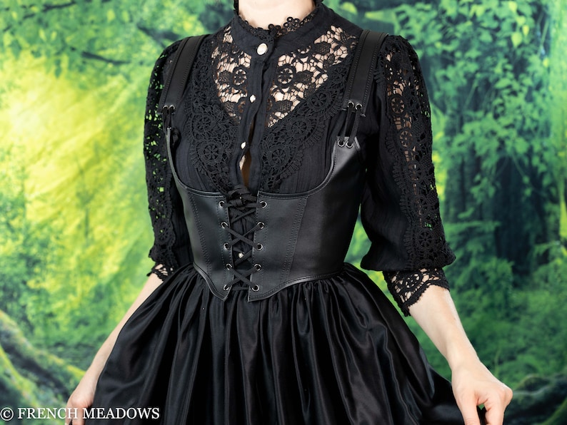 Black leather underbust corset belt styled with lace top and flowing skirt against green forest backdrop