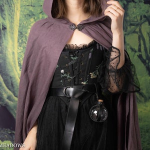 Potion bottle holder with black leather strap attached to black embroidered corset and purple cloack, displaying clear spherical vial