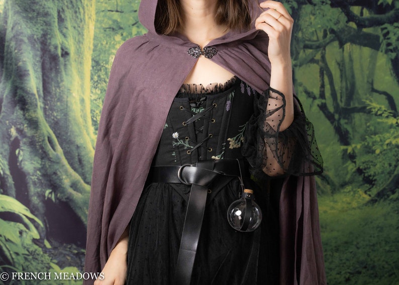 Potion bottle holder with black leather strap attached to black embroidered corset and purple cloack, displaying clear spherical vial