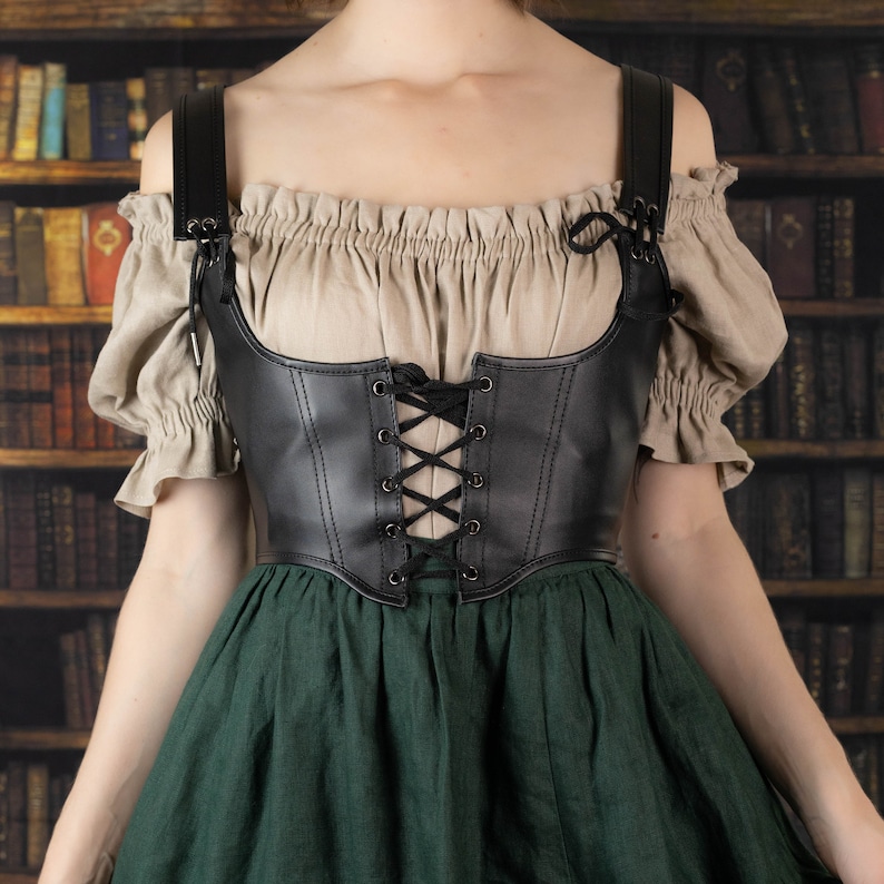 Leather underbust corset belt shown on mannequin with peasant blouse and green dress against vintage bookshelf background