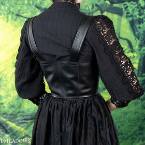 May include: Black leather corset with adjustable straps. The corset has a fitted bodice and a straight skirt. The corset is worn over a black blouse with lace trim.