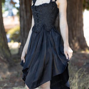 Puede incluir: Vestido negro con corpi&ntilde;o estilo cors&eacute; y falda asim&eacute;trica. El corpi&ntilde;o presenta un frente con cordones y adornos decorativos. El vestido tiene tirantes delicados y una est&eacute;tica rom&aacute;ntica y g&oacute;tica, adecuado para ocasiones especiales.