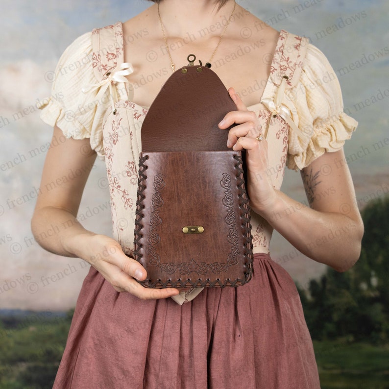 Brown leather Elven Medieval Belt Pouch with ornate scroll design, held against vintage dress, showing clasp and stitching detail