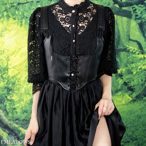 Leather underbust corset belt styled with black lace top and flowing skirt against forest backdrop