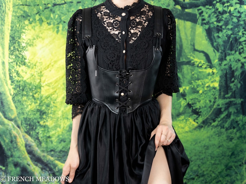 Leather underbust corset belt styled with black lace top and flowing skirt against forest backdrop