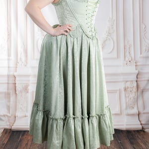 Puede incluir: Un vestido cors&eacute; verde claro con un estampado floral. El vestido presenta un corpi&ntilde;o con cordones, una falda amplia con volantes y una camiseta interior blanca. El vestido se combina con bailarinas marrones. El vestido es aproximadamente hasta la rodilla.