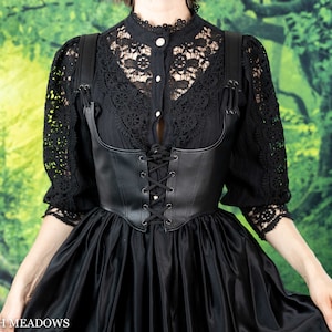 Leather underbust corset belt styled with black lace top and flowing skirt against green forest backdrop