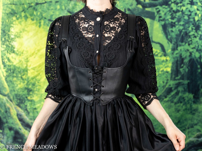 Leather underbust corset belt styled with black lace top and flowing skirt against green forest backdrop