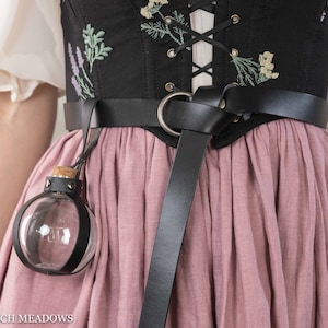 Potion bottle holder with black leather strap attached to embroidered corset and pink skirt, displaying clear spherical vial