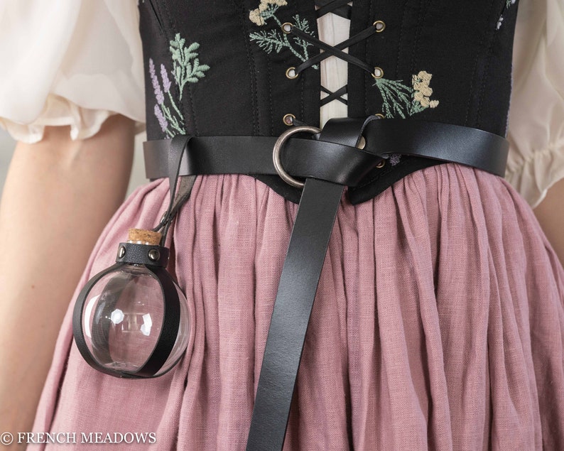 Potion bottle holder with black leather strap attached to embroidered corset and pink skirt, displaying clear spherical vial