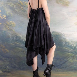 Puede incluir: Vestido negro asim&eacute;trico con tirantes finos y un lazo en la espalda. El vestido se combina con botines negros con un tac&oacute;n peque&ntilde;o. El fondo presenta un paisaje suave y pict&oacute;rico.