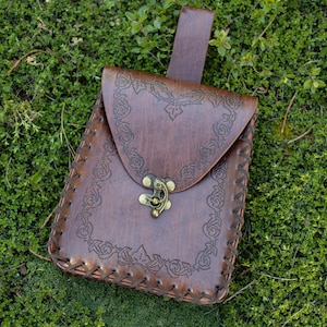 Elven Medieval Belt Pouch with ornate scroll design, brown leather texture, brass clasp, displayed on green grass background
