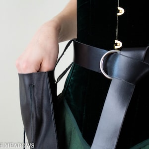Drawstring pouch in black vegan leather shown attached to medieval-style belt with silver buckle against green and black costume