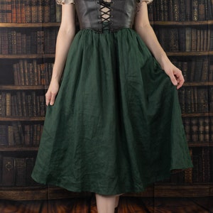 Leather underbust corset belt paired with cream peasant top and forest green skirt against vintage library background