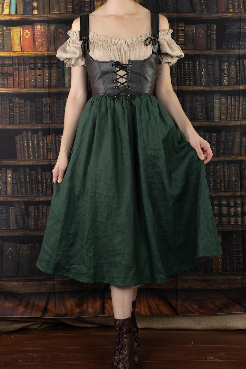 Leather underbust corset belt paired with cream peasant top and forest green skirt against vintage library background