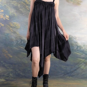 Puede incluir: Vestido negro asim&eacute;trico con tirantes finos y escote con volantes. El vestido tiene un dobladillo fluido en forma de pa&ntilde;uelo y se combina con botas negras con cordones. El fondo es un paisaje pintado.