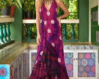 May include: A sleeveless magenta and purple tie-dye maxi dress featuring a deep V-neckline, a halter-style bodice, and a ruffled high-low hemline. The fabric is decorated with a repeating pattern of white circular floral motifs.