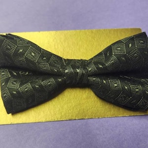 May include: A black bow tie with a geometric pattern on a gold background.