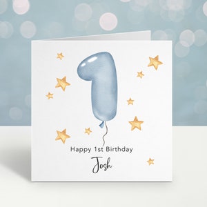 May include: A white card with a blue number one balloon and gold stars. The text "Happy 1st Birthday Josh" is printed on the card.
