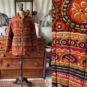 Puede incluir: Una chaqueta acolchada vintage con un patrón geométrico marrón, naranja y rojo. La chaqueta está en un maniquí y tiene una cremallera.