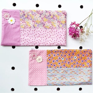 May include: Two rectangular fabric pouches with floral and polka dot patterns. One pouch has a pink polka dot section with crochet flowers. The other pouch has a section with orange flowers and blue wave pattern.