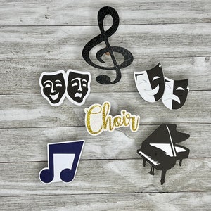May include: Black and white paper cutouts of a treble clef, two masks, a piano, and a musical note. The word "choir" is written in gold glitter letters.