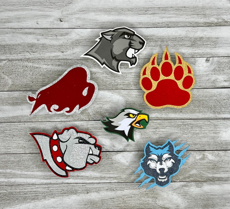 K&ouml;nnte beinhalten: Sechs verschiedene tierf&ouml;rmige, glitzernde Filzapplikationen. Die Applikationen sind ein roter Bulle, ein grauer Panther, ein roter B&auml;renpfotenabdruck, ein grau-wei&szlig;er Bulldogge, ein blauer Wolf und ein gelb-wei&szlig;er Adler.