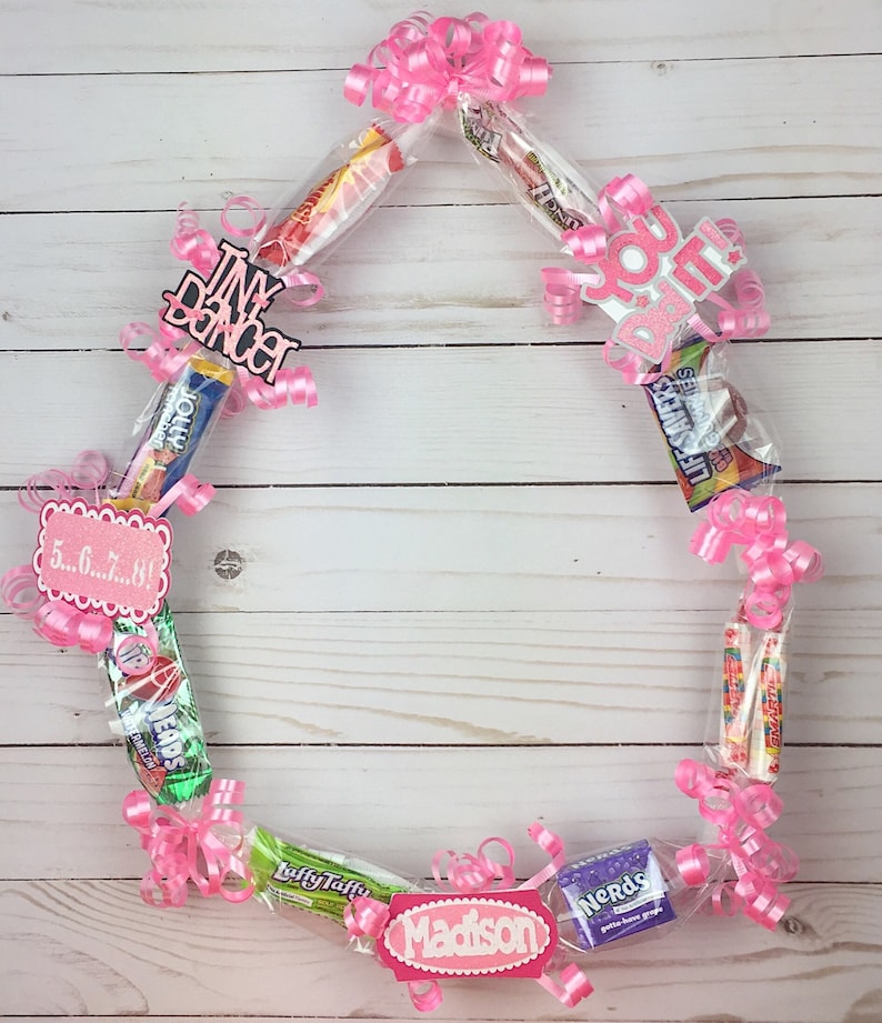 May include: A candy lei constructed from various individually wrapped sweets including Jolly Rancher, Life Savers, Nerds, and Laffy Taffy, accented with pink curling ribbon and decorative cardstock cutouts reading Tiny Dancer, You Did It, 5...6...7...8!, and Madison.