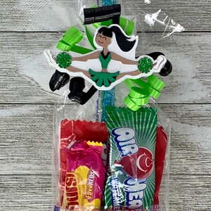 May include: A clear plastic gift bag containing assorted candy including Twizzlers, AirHeads, and Swedish Fish. The bag is decorated with a die-cut paper cheerleader figure in a green and black uniform holding green pom-poms, accented with green ribbons.