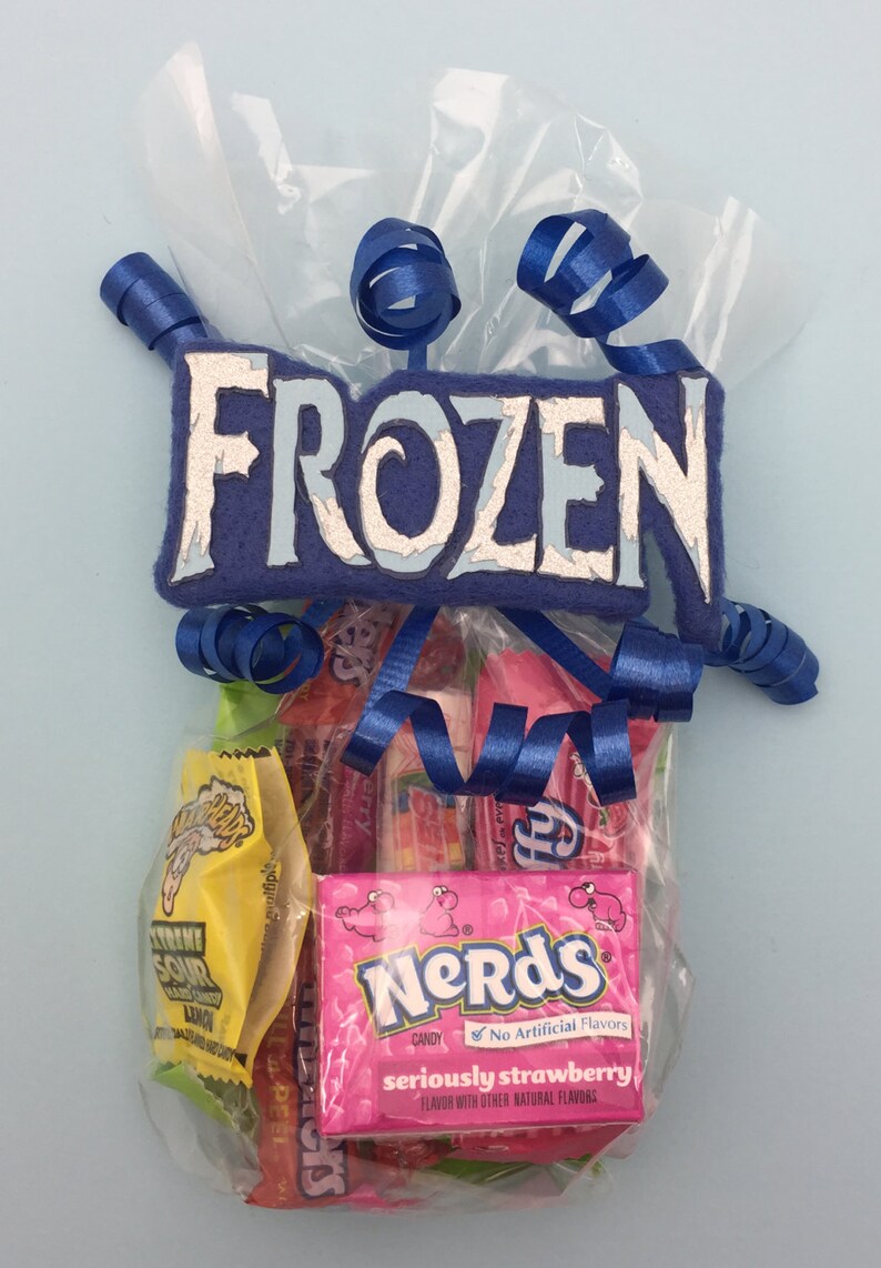 May include: A clear plastic gift bag filled with assorted sweets, including a pink box of Nerds Seriously Strawberry and a yellow packet of Extreme Sour hard candy. The bag is topped with a blue felt sign reading FROZEN and blue ribbons.