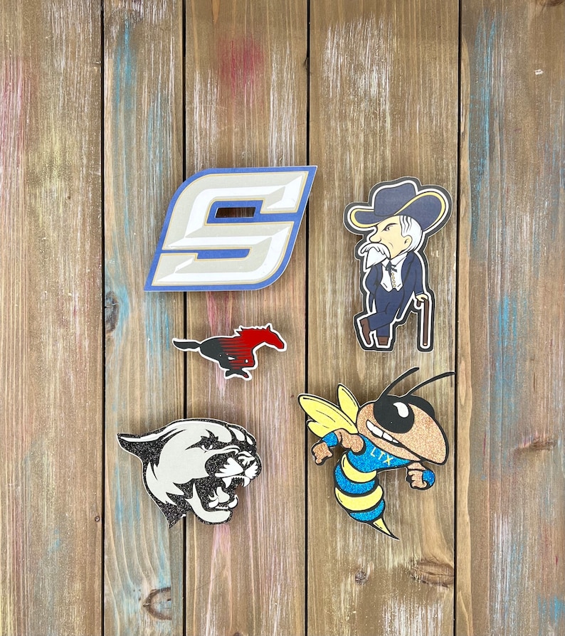 K&ouml;nnte beinhalten: F&uuml;nf verschiedene Schulmaskottchen-Logos auf einem Holzgrund. Die Logos sind eine blaue und wei&szlig;e Nummer "9", ein rotes und schwarzes Pferd, ein wei&szlig;er Pantherkopf, eine gelbe und blaue Biene mit dem Text "LTX" und ein Cartoon-Mann mit wei&szlig;em Bart, der einen blauen Anzug und einen blau-wei&szlig;en Cowboyhut tr&auml;gt.