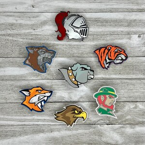 K&ouml;nnte beinhalten: Sieben bunte B&uuml;gelbilder mit verschiedenen Tier- und Maskottchen-Designs. Die Patches zeigen einen Ritter, einen Wolf, eine Bulldogge, einen Fuchs, einen Adler, einen Tiger und einen Kobold.