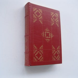 May include: A red book with gold decorative patterns. The cover features a repeating geometric design. The spine has the title "LITTLE BOOKS" in gold lettering. The book is set against a white background.