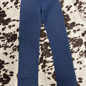 May include: A pair of classic blue denim jeans. The jeans have a straight leg cut, a button and zipper closure, and classic five-pocket styling. The jeans are displayed on a cowhide patterned surface.